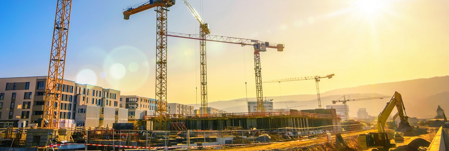 Large construction site including several cranes, with clear sky and the sun